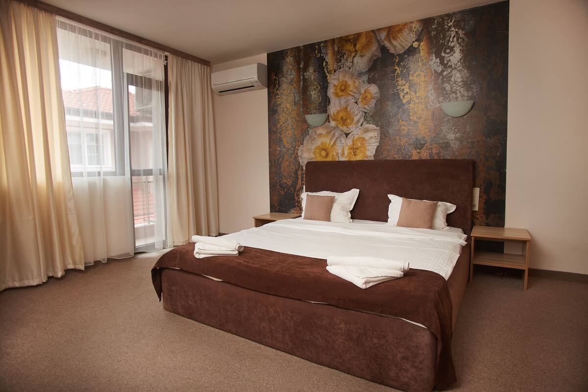 A bedroom with a large bed, a view of the outdoors through a window, and a decorative wall piece.