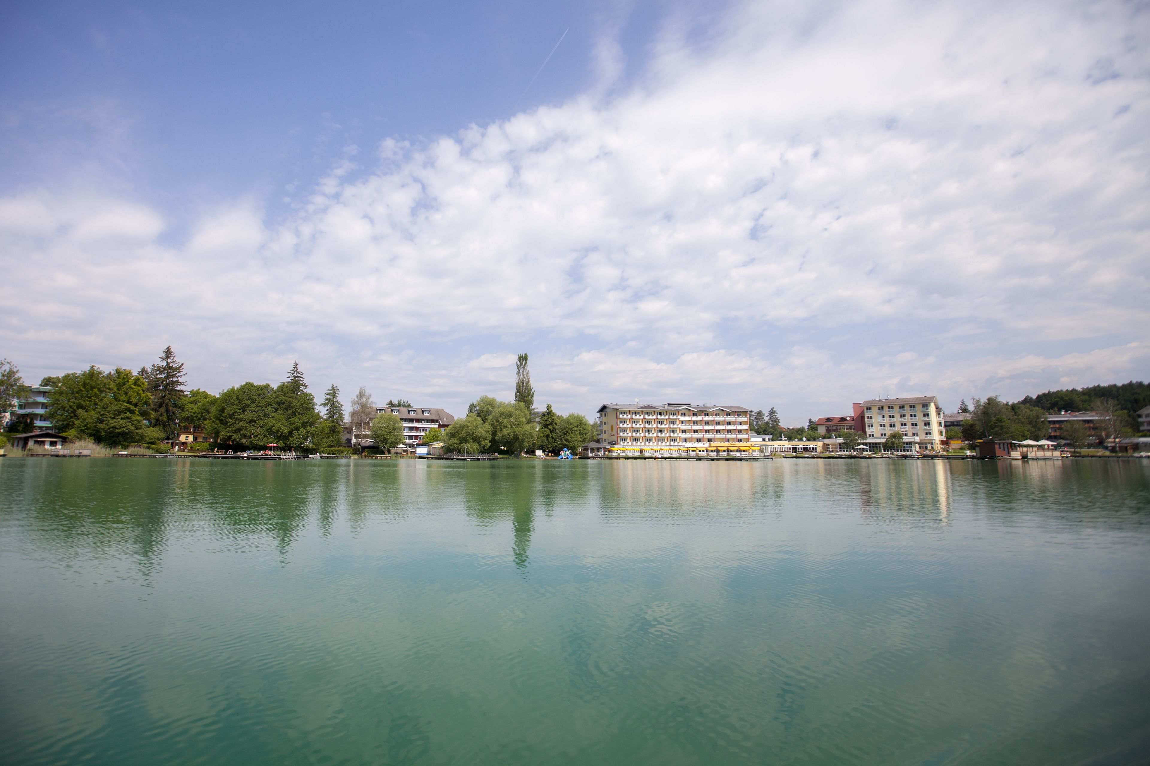 A calm lake with buildings and trees in the background.