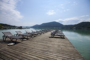 A wooden pier with rows of empty lounge chairs facing a calm lake, surrounded by hills. - See & GenussHotel Silvia (Sankt Kanzian am Klopeiner See)