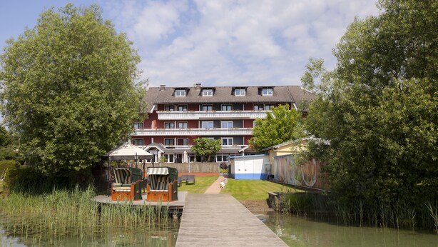 A multi-story residential building with a wooden dock leading to a grassy area. - See & GenussHotel Silvia (Sankt Kanzian am Klopeiner See)