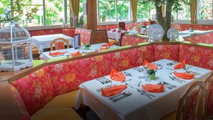 A restaurant with booths and tables, some with orange napkins, and a birdcage on a table. - See & GenussHotel Silvia (Sankt Kanzian am Klopeiner See)