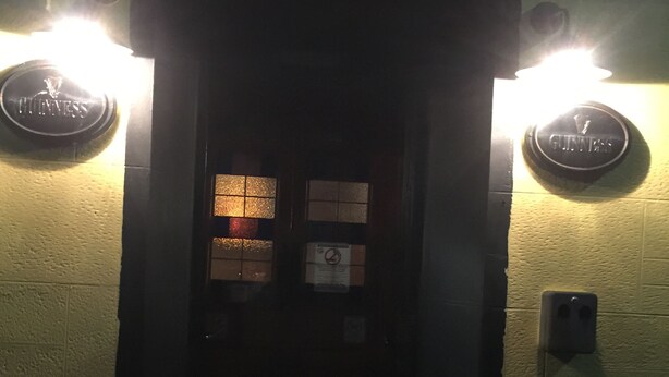 Une entrée sombre, de part et d’autre de laquelle se trouvent deux enseignes lumineuses portant l’inscription « GUINNESS ».