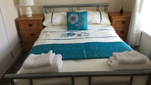 Un lit bien fait, avec une couette bleue et blanche, deux oreillers et une table de chevet sur laquelle se trouve une lampe.