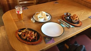 Une table à manger avec un verre de bière, une assiette de nourriture et un bol de rondelles d’oignon.