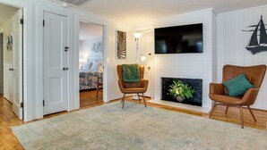 Un salon avec une cheminée, un téléviseur fixé au mur et deux fauteuils.