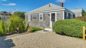 Une maison de plain-pied aux murs recouverts de bardeaux gris, dotée d’un porche à l’avant et d’une allée en gravier.