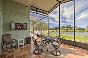 A covered patio with a table and chairs, a dartboard, and a view of a lake and houses in the background. - Lakefront Brandon Home w/ Patio & Screened Lanai! (Brandon)