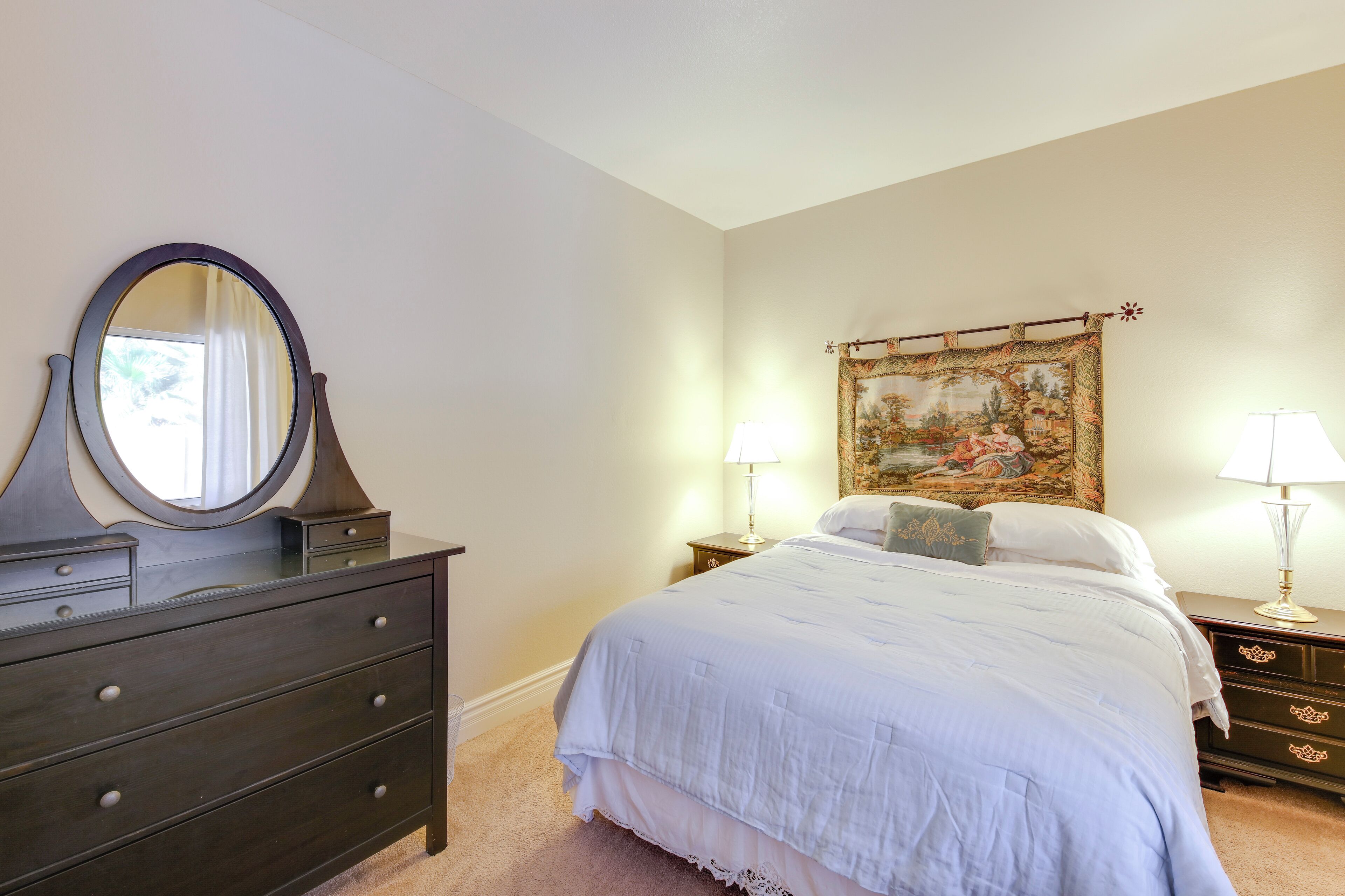 Une chambre à coucher comprenant un lit, une commode, un miroir et deux lampes de chevet.