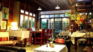 Une pièce chaleureuse comprenant une table à manger, des chaises, un canapé et une table basse. Des fenêtres offrent une vue sur la verdure environnante.