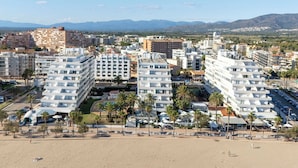Un paisaje urbano costero con edificios modernos, una playa y montañas al fondo.