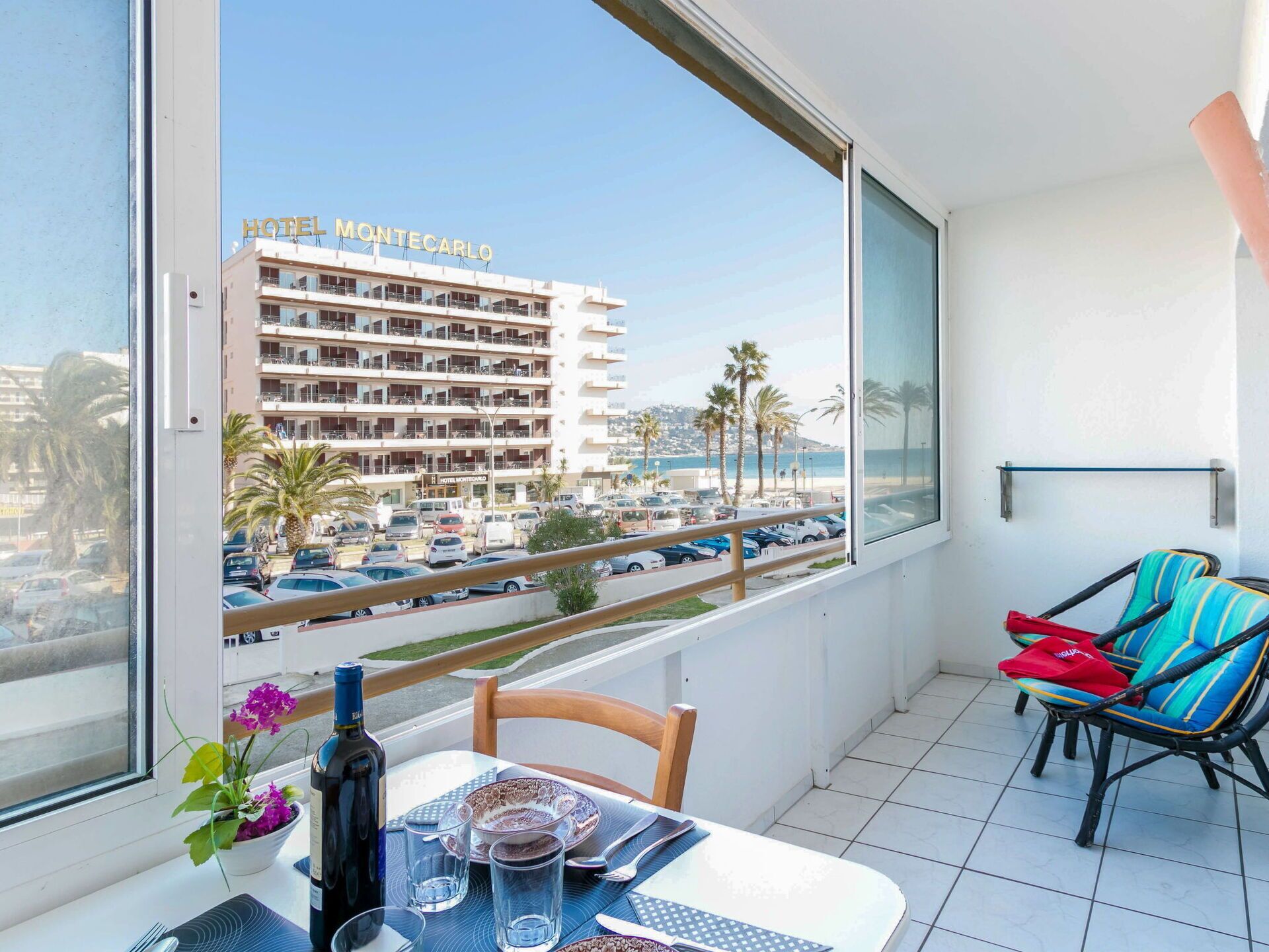 Un balcón con una mesa preparada para dos personas, una silla y vistas al Hotel Montecarlo y un estacionamiento.