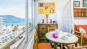 Un balcón con vista a la playa y al océano, una mesa de madera con juego de té y un cuadro en la pared.