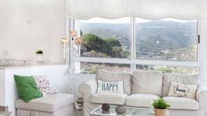 A cozy living room with a beige sofa set, a glass coffee table, and a view of a mountainous landscape through large windows. - Beautiful apartment for 4 people with WIFI, TV and terrace (Tossa De Mar)
