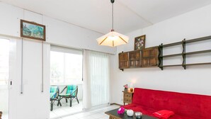 A living room with a red sofa, a wooden coffee table with decorative items, a hanging light fixture, and a view through a glass door to an outdoor area with chairs.