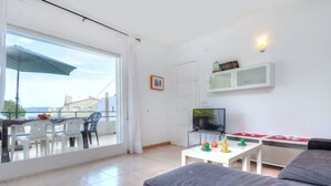 A modern living room with a grey sofa, a dining table with chairs, a TV on a stand, and a balcony with an umbrella. - Lovely apartment for 5 people with WIFI, TV, terrace and pets allowed (Grifeu)