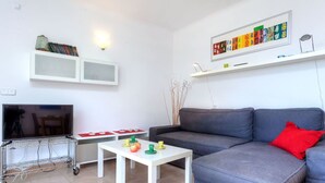 A modern living room with a grey sofa, a white coffee table, a flat-screen TV, and a shelf with decorative items. - Lovely apartment for 5 people with WIFI, TV, terrace and pets allowed (Grifeu)