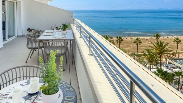 Un balcon avec une table dressée pour le dîner, donnant sur une plage bordée de palmiers et sur l’océan.