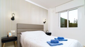 A neatly made bed with a white duvet, a bedside table with a lamp, and a window with a view of greenery. - Beautiful apartment for 4 people with WIFI, A/C, pool, TV and patio (Teulada)