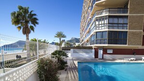 Ein Hotelpoolbereich mit freiem Blick auf den Ozean, einer Palme und einem Gebäude mit Balkonen.