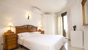 Ein Schlafzimmer mit einem hölzernen Bett, zwei Nachttischen mit Lampen, einer Wand-Klimaanlage und einem Fenster mit Vorhängen.