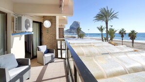 Ein Balkon mit einem Korbstuhl, einer weißen Klimaanlage und Blick auf Strand und Berge.