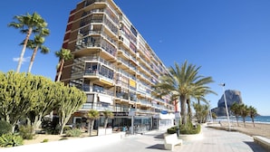 Ein mehrstöckiges Hotel mit Balkonen, Blick auf den Strand und Palmen.