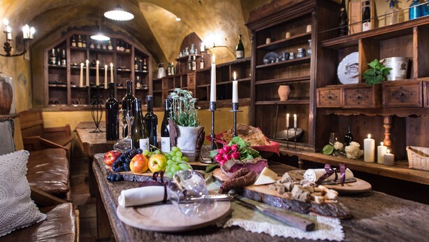 Un comedor rústico con una mesa de madera dispuesta para una comida, rodeada de estanterías llenas de botellas y copas.