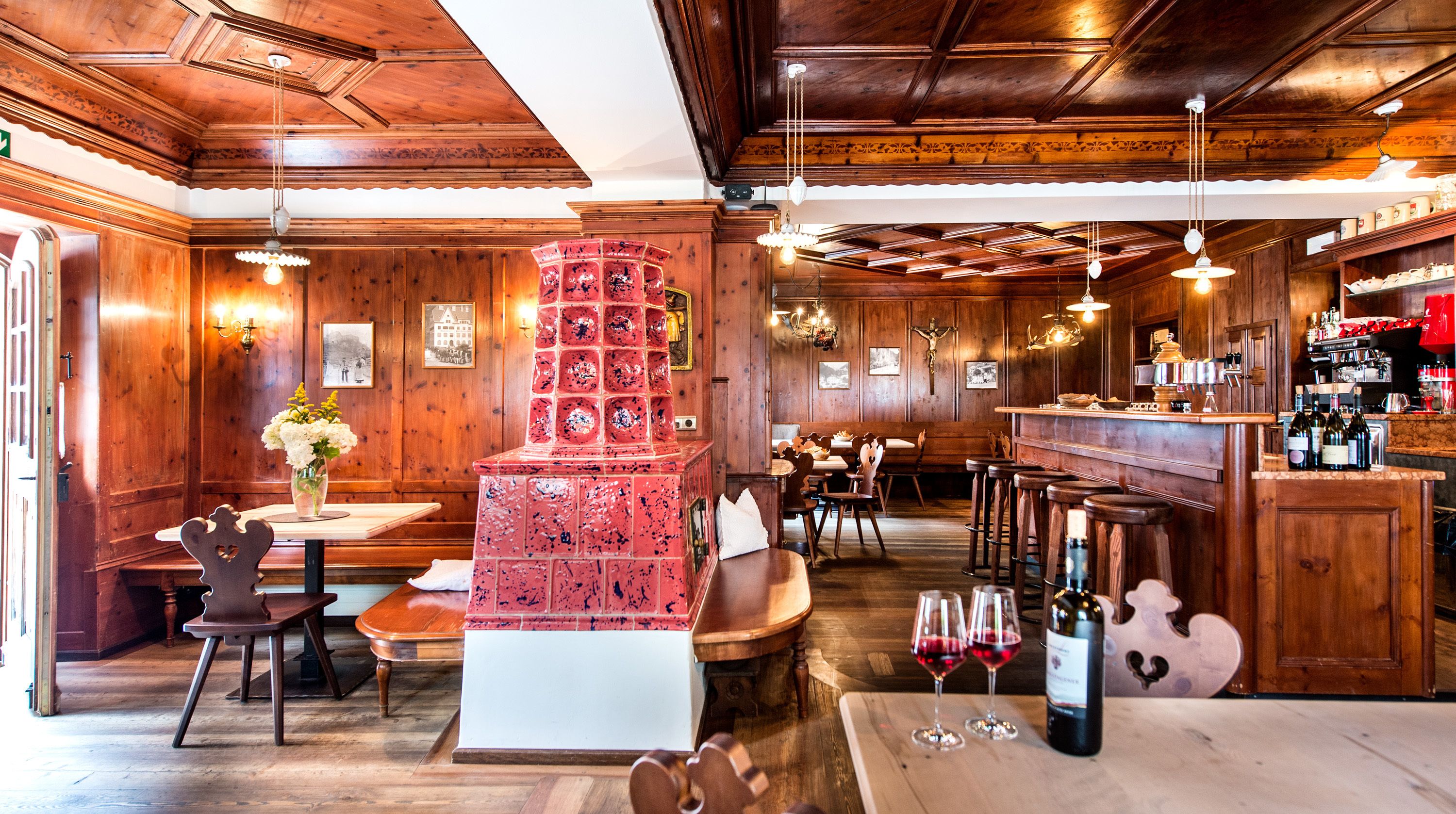 Un restaurante acogedor con interiores de madera, una chimenea central de ladrillo rojo y una zona de bar con botellas de vino.