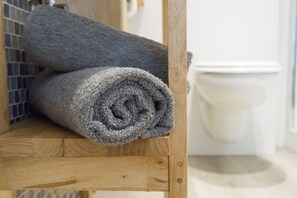 Una toalla gris enrollada sobre un estante de madera en un baño.
