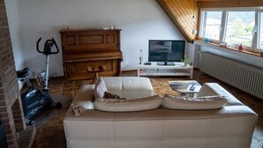 Un salon avec un canapé blanc, un meuble en bois, une télévision et une fenêtre donnant sur des maisons.