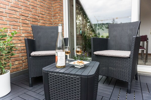 Un patio con dos sillones de mimbre, una mesa, una botella de vino y una copa de vino.
