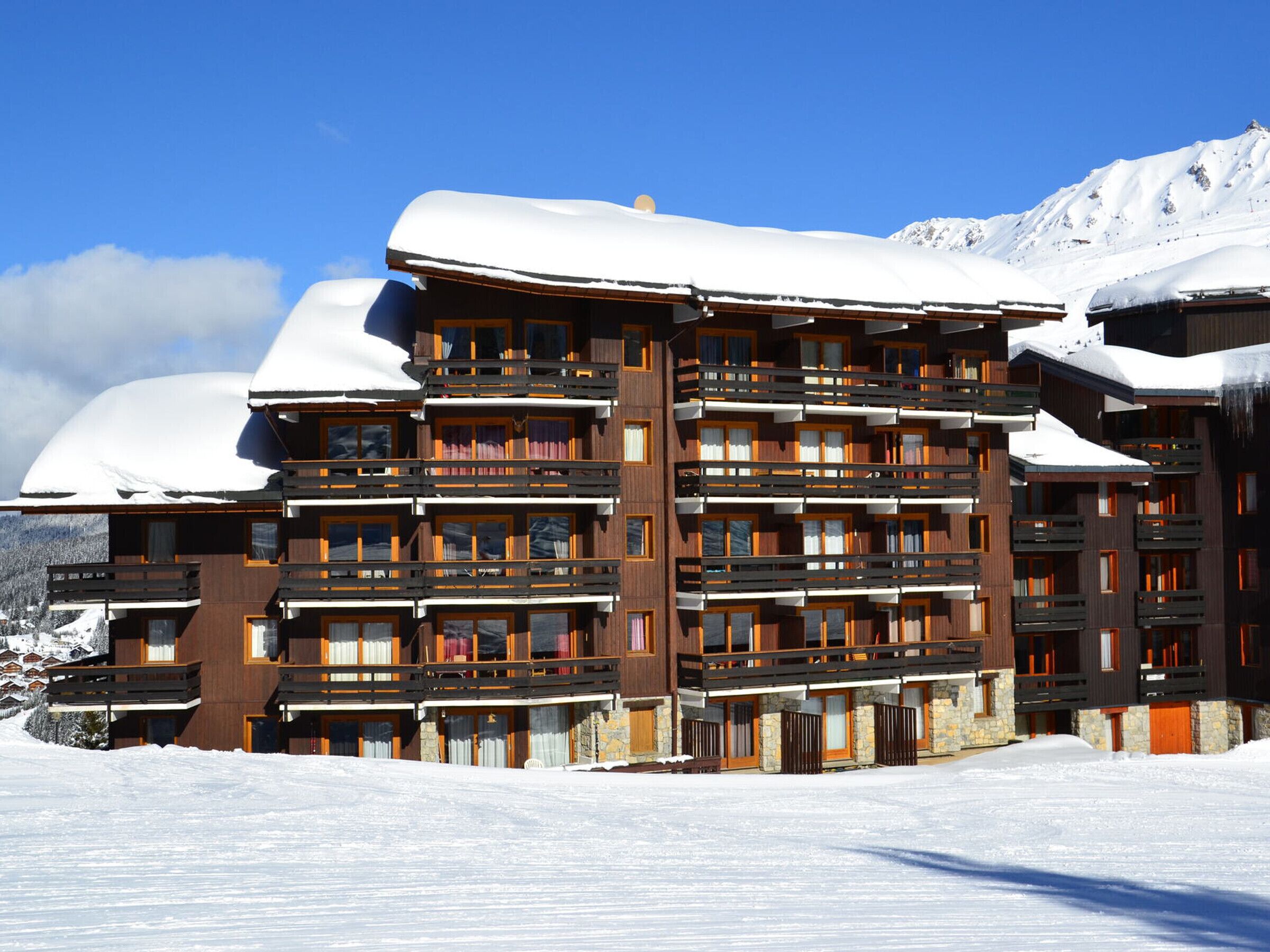 A multi-story hotel with balconies and a snow-covered roof, surrounded by mountains.
