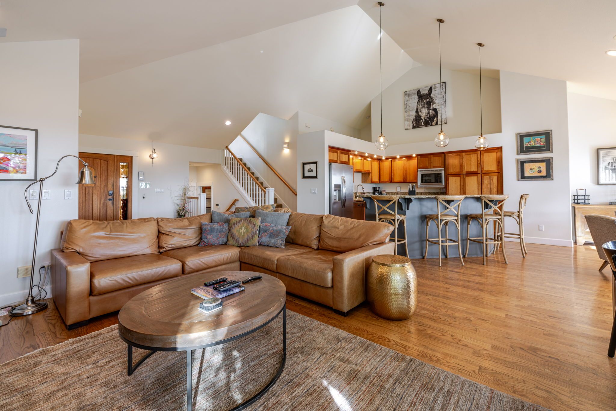 A spacious living room with a leather sectional sofa, a coffee table, and a kitchen area with wooden cabinets and a bar.