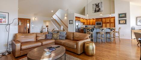 A spacious living room with a leather sectional sofa, a coffee table, and a kitchen area with wooden cabinets and a bar.