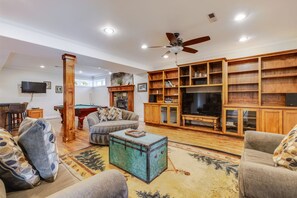 A spacious living room with a pool table, comfortable seating, a television, and a fireplace.