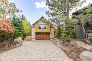 A two-story house with a garage, surrounded by trees and a paved driveway.