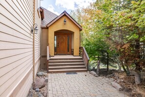 A wooden house with a front porch, steps leading to a door, and a stone pathway.