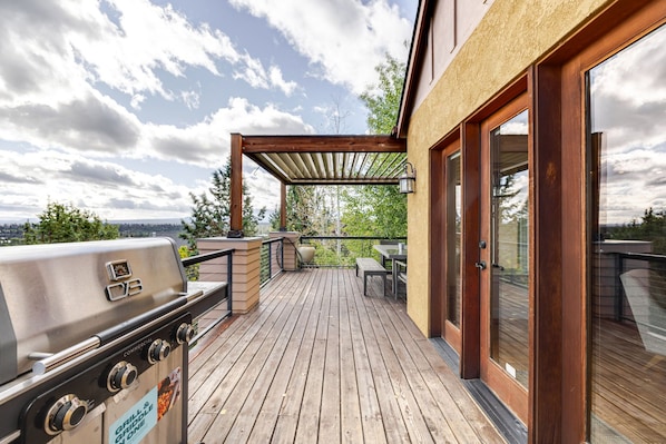 Una terraza de madera con una parrilla, una mesa y una pérgola.