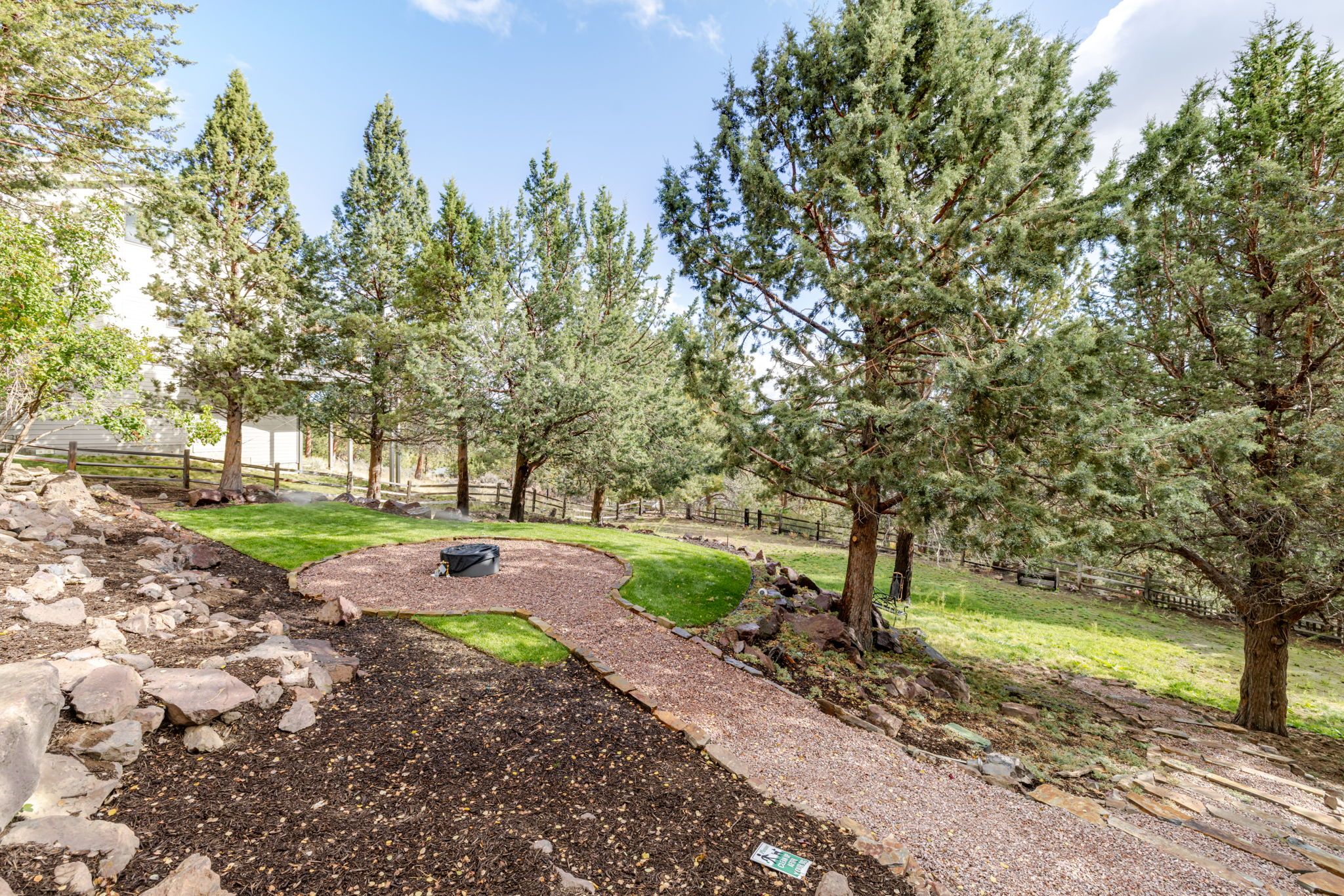 A landscaped garden with a winding gravel path, surrounded by mature trees and a grassy area.