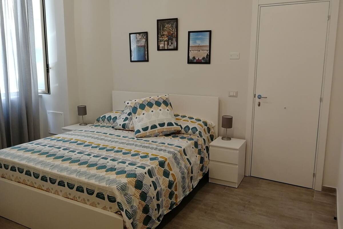 Un dormitorio ordenado con una cama, dos mesitas de noche y tres cuadros en la pared.