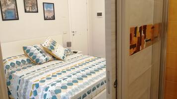 A bedroom with a bed, pillows, a bedside table, and a door.