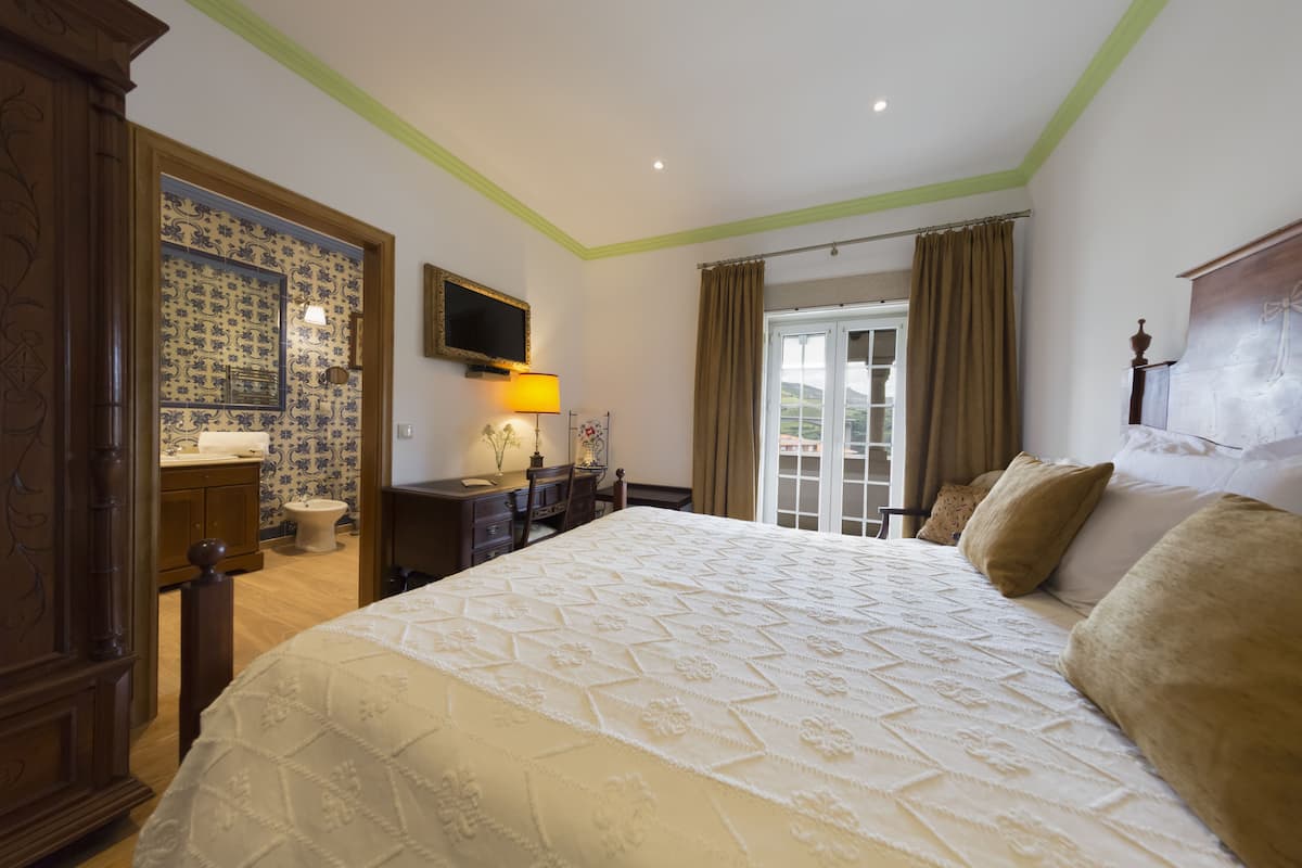 Ein Schlafzimmer mit einem großen Bett, einem Fernseher, einem Schreibtisch mit Lampe und einem Badezimmer mit Toilette und Waschbecken.