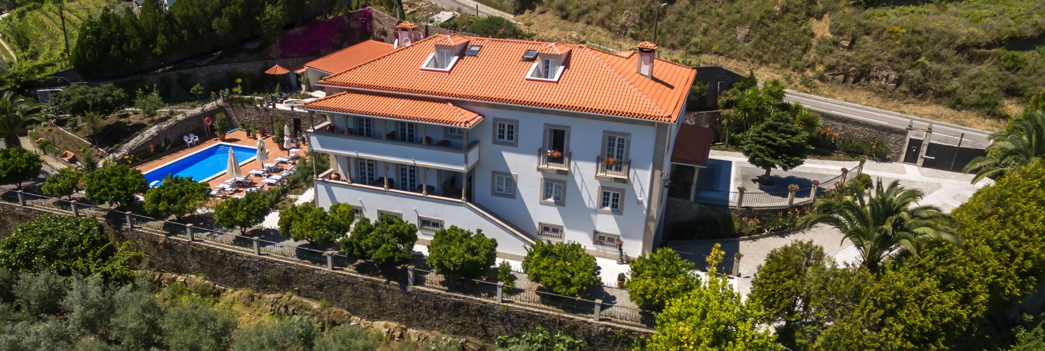 Una casa de dos pisos con piscina, un muro de contención de piedra y un jardín.