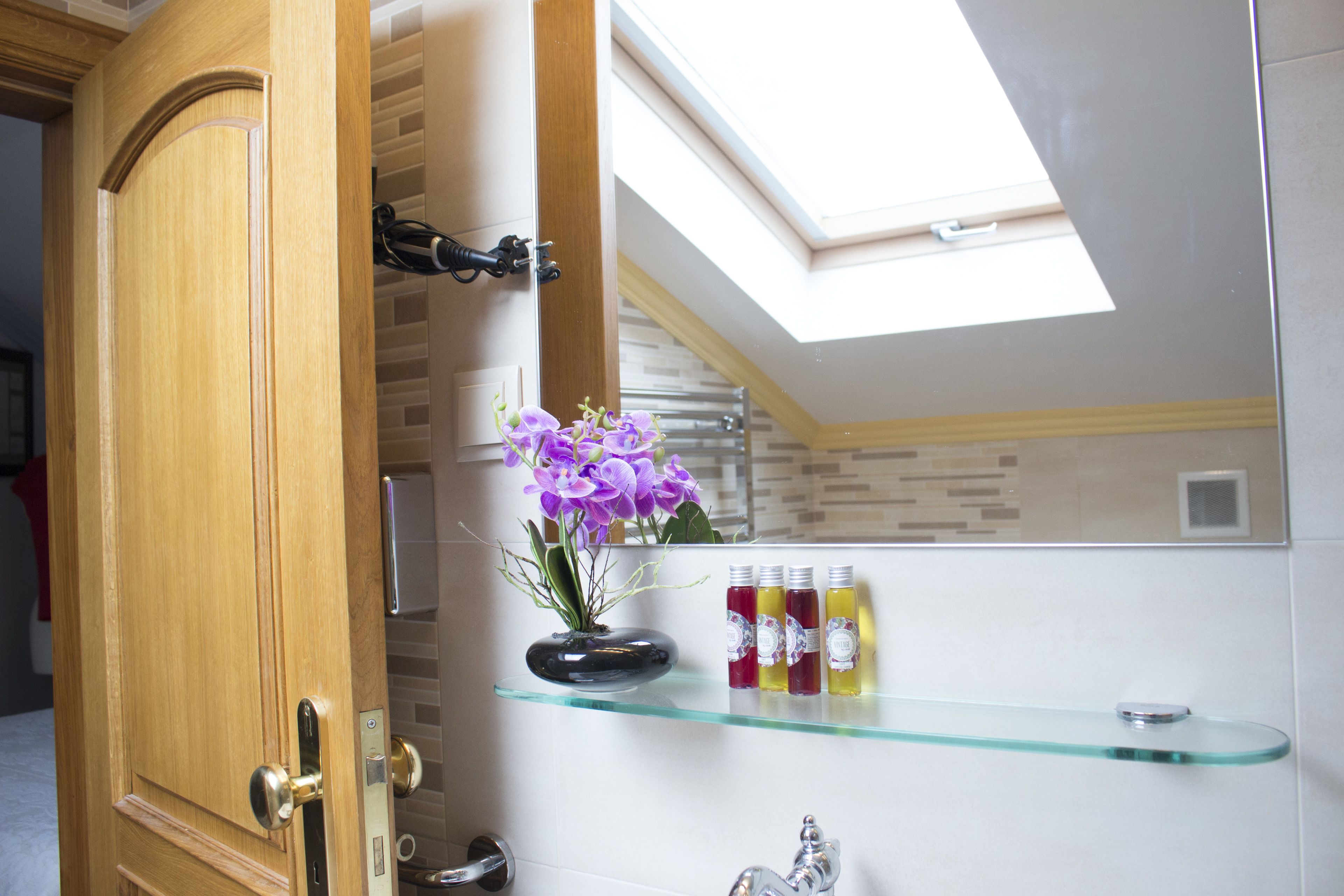 A bathroom with a wooden door, a glass shelf with toiletries, and a skylight.