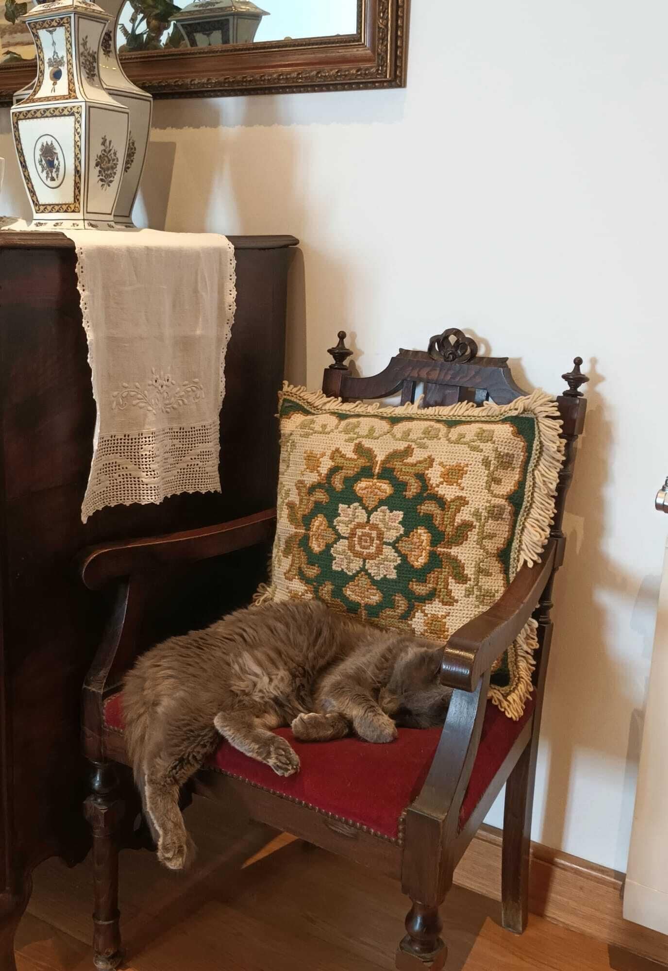 Una silla con un cojín floral y un mantel de encaje sobre una mesa de madera.