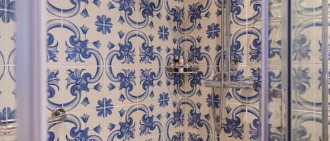 A bathroom with blue floral tiles, a glass shower enclosure, and a visible showerhead.