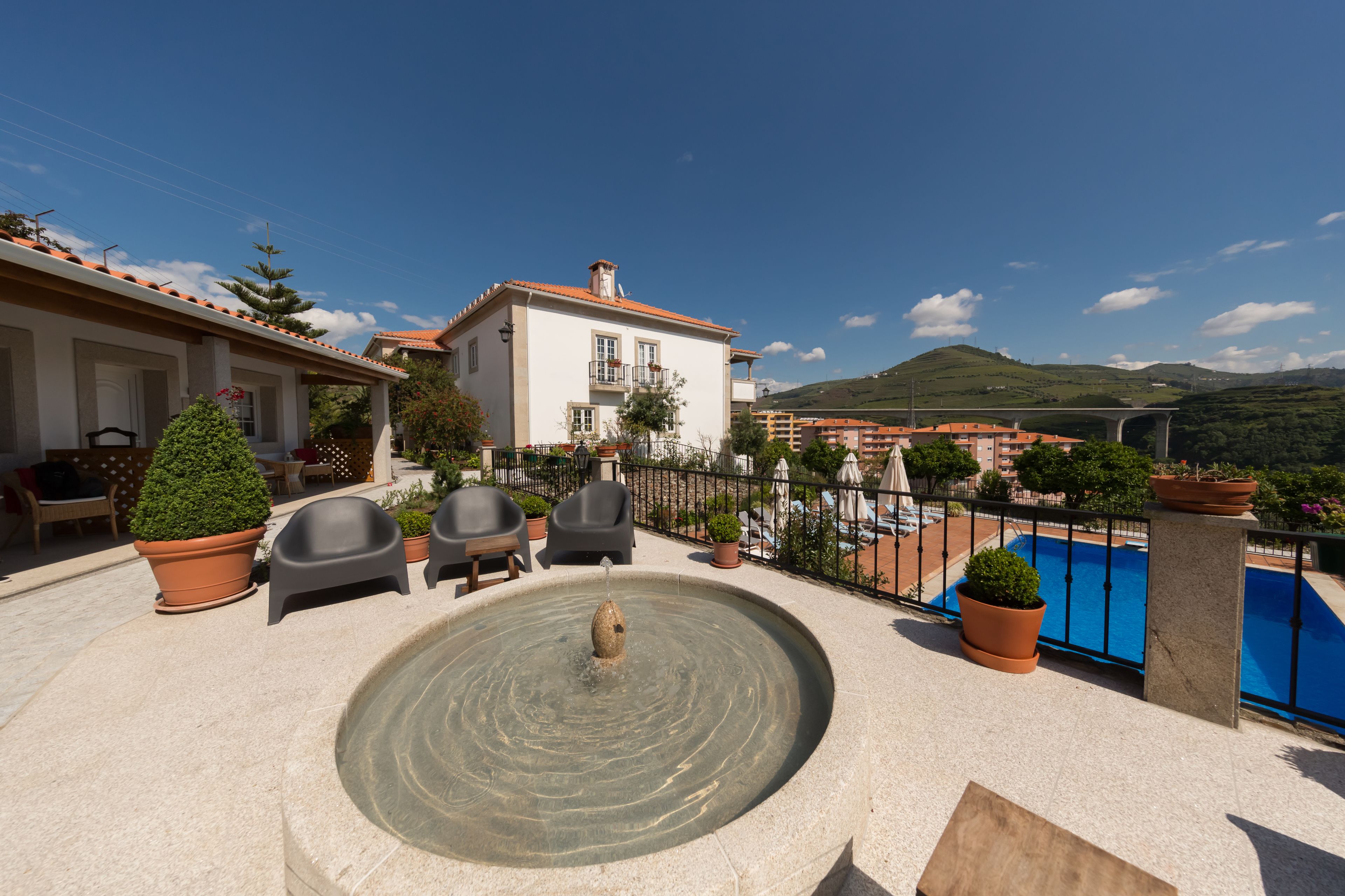 Una terraza en la azotea con una fuente, mobiliario exterior y vistas a una piscina y colinas.