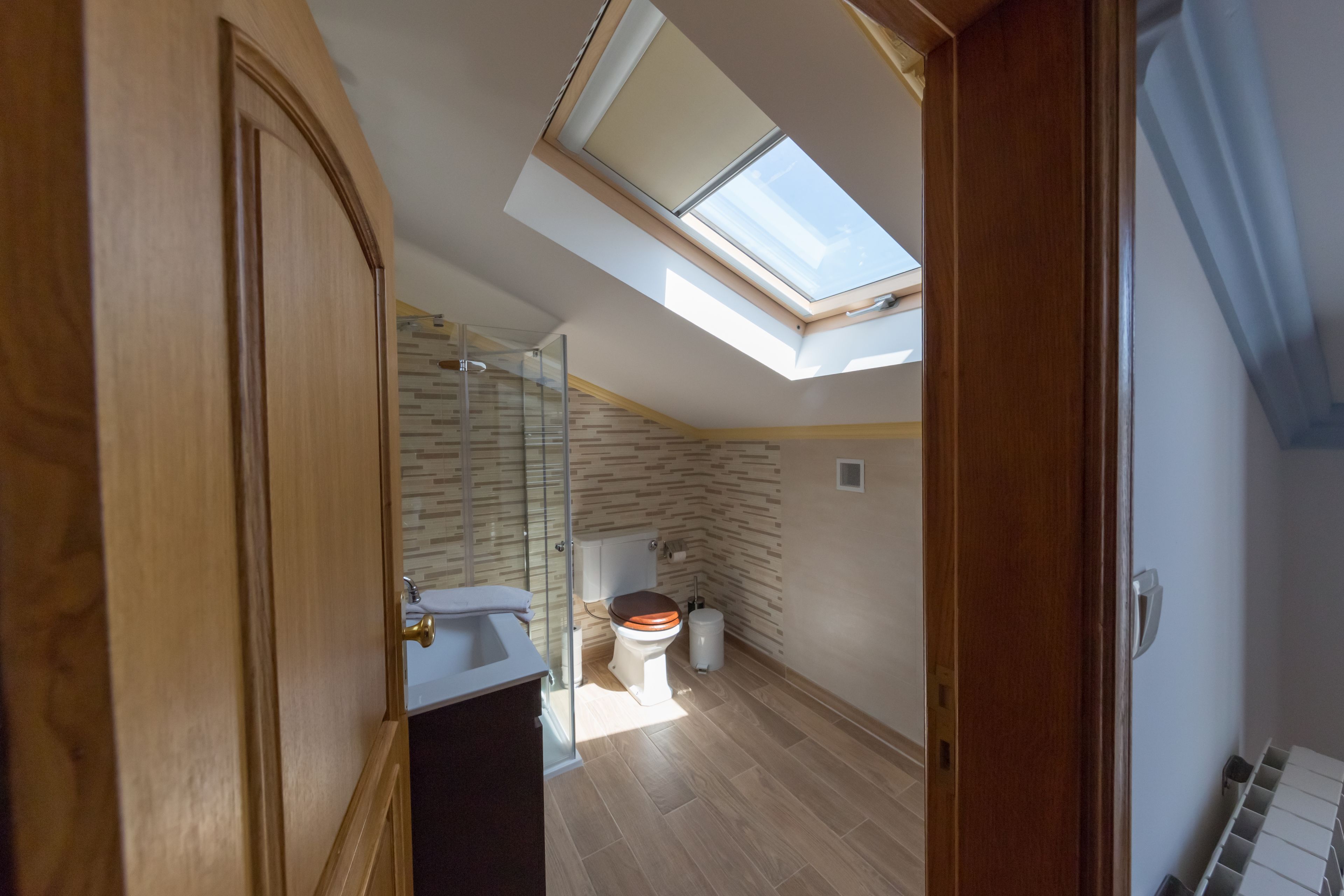 Une salle de bain moderne dotée d’un puits de lumière, d’un plancher en bois et d’une cabine de douche en verre.