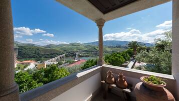 A balcony with terracotta pots and a view of a bridge and green hills.