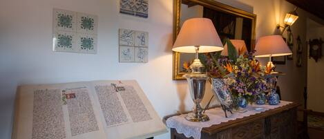 A room with a table displaying a book, two lamps, a mirror, and wall decorations.